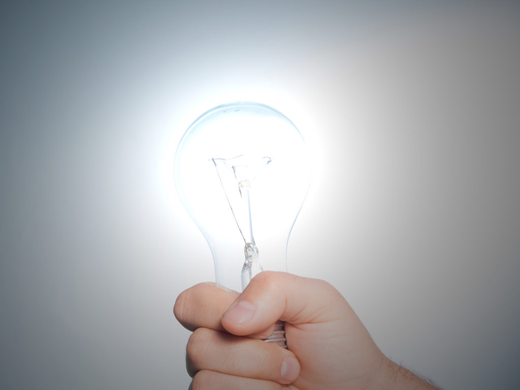 Hand holding an incandescent light bulb on blue background.